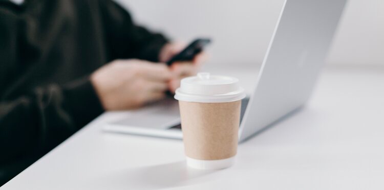 Cup of coffee in foreground, laptop in background