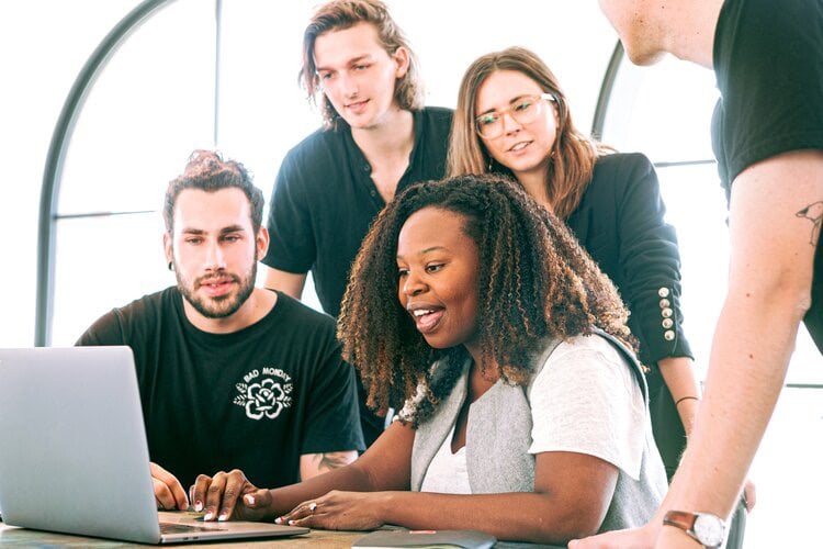 Multiple people gathered around a single laptop 